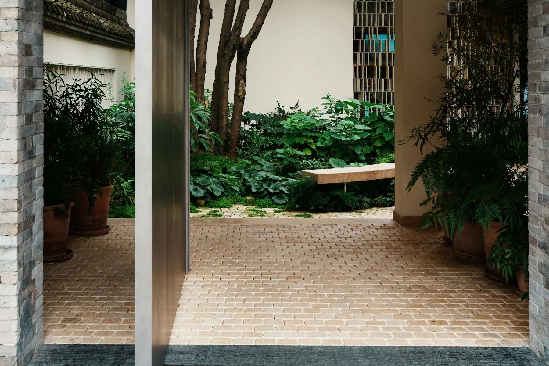 A modern grey-brick entrance frames a planted courtyard and stone walkway at Taikoo Li, Chengdu.